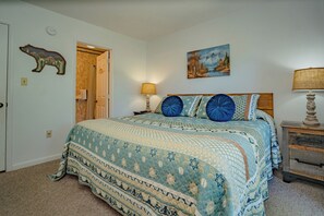 A bedroom with a bed, a nightstand, a lamp, a painting, and a door.