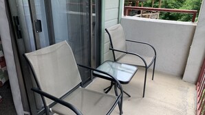 A balcony with two chairs and a table, a sliding glass door, and a view of a building and trees. - Laurel Inn 411 is a beautiful condo with private balcony close to downtown (Gatlinburg)