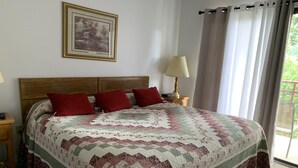 A neatly made bed with a patterned quilt, a wooden headboard, a nightstand with a lamp, and a framed picture on the wall. - Laurel Inn 411 is a beautiful condo with private balcony close to downtown (Gatlinburg)
