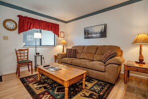 A living room with a brown sofa, a wooden coffee table, a patterned rug, a clock, and a framed picture on the wall.