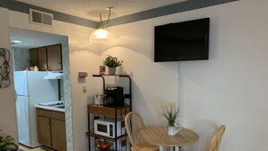 A compact kitchen with a refrigerator, microwave, and coffee maker on a cart, a dining table with chairs, and a TV mounted on the wall. - Laurel Inn 411 is a beautiful condo with private balcony close to downtown (Gatlinburg)