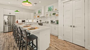 A modern kitchen with white cabinetry, a central island, bar stools, and a stainless steel refrigerator.