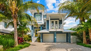 A two-story house with a white and blue exterior, a front garage, and a gravel driveway.