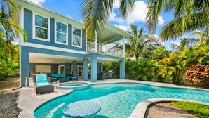 A two-story house with a swimming pool, outdoor furniture, and tropical landscaping.