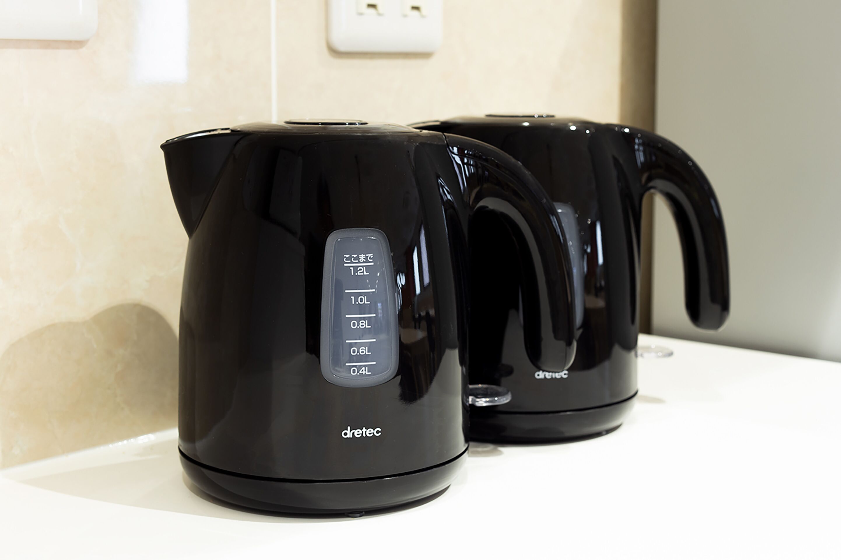 Two black electric kettles with measurement markings on a white countertop.