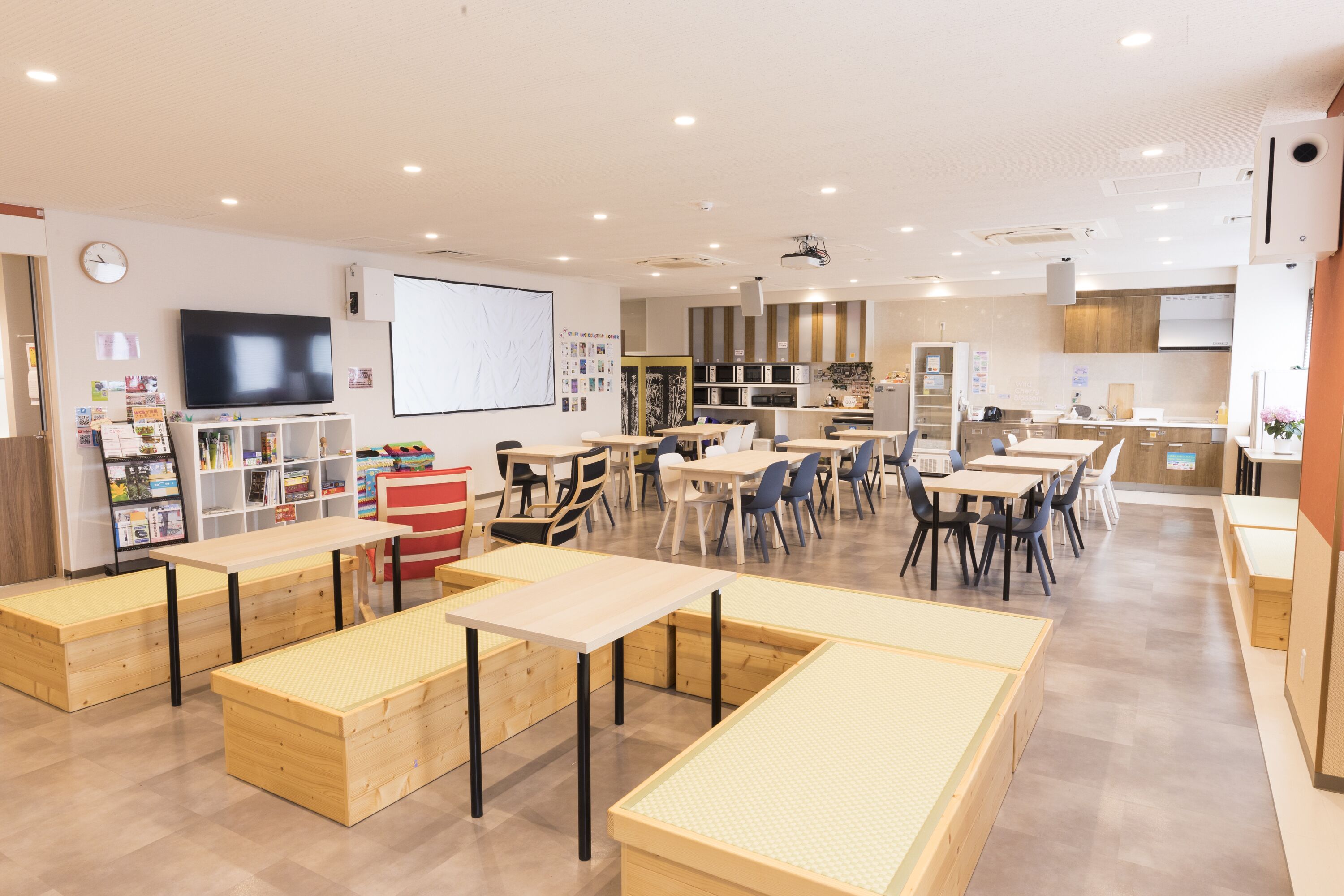 A spacious classroom with tables and chairs, a projector screen, and a whiteboard.