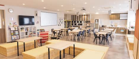 A spacious classroom with tables and chairs, a projector screen, and a whiteboard.