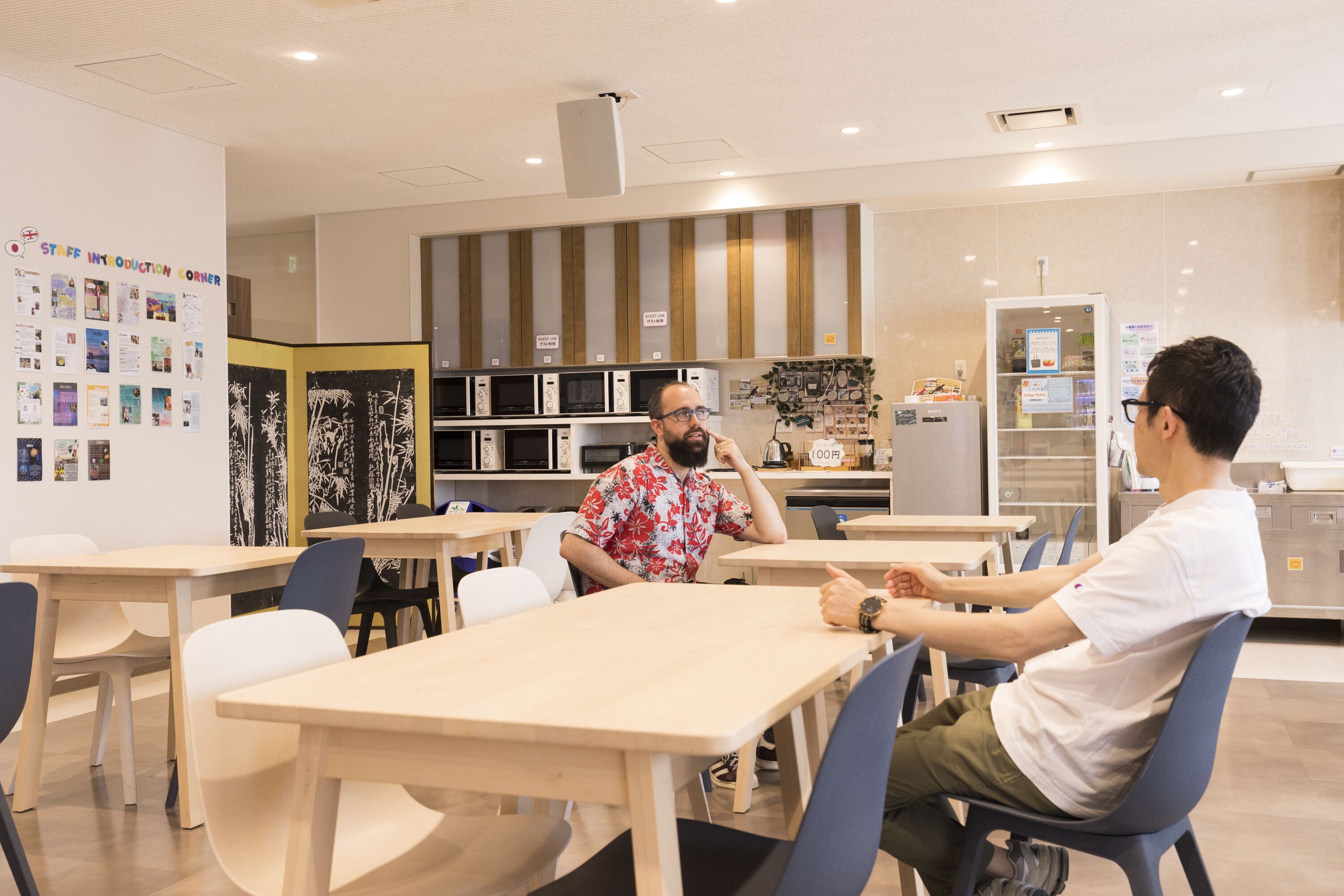 Un'area cucina moderna con tavoli e sedie in legno, un frigorifero e un forno a microonde.