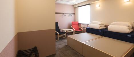 A hotel room with a bed, a red chair, a small table, and a window with blinds.