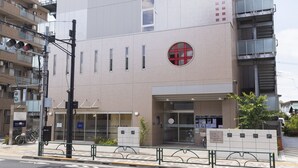 A modern building with a prominent vertical window, a circular logo, and a gated entrance.