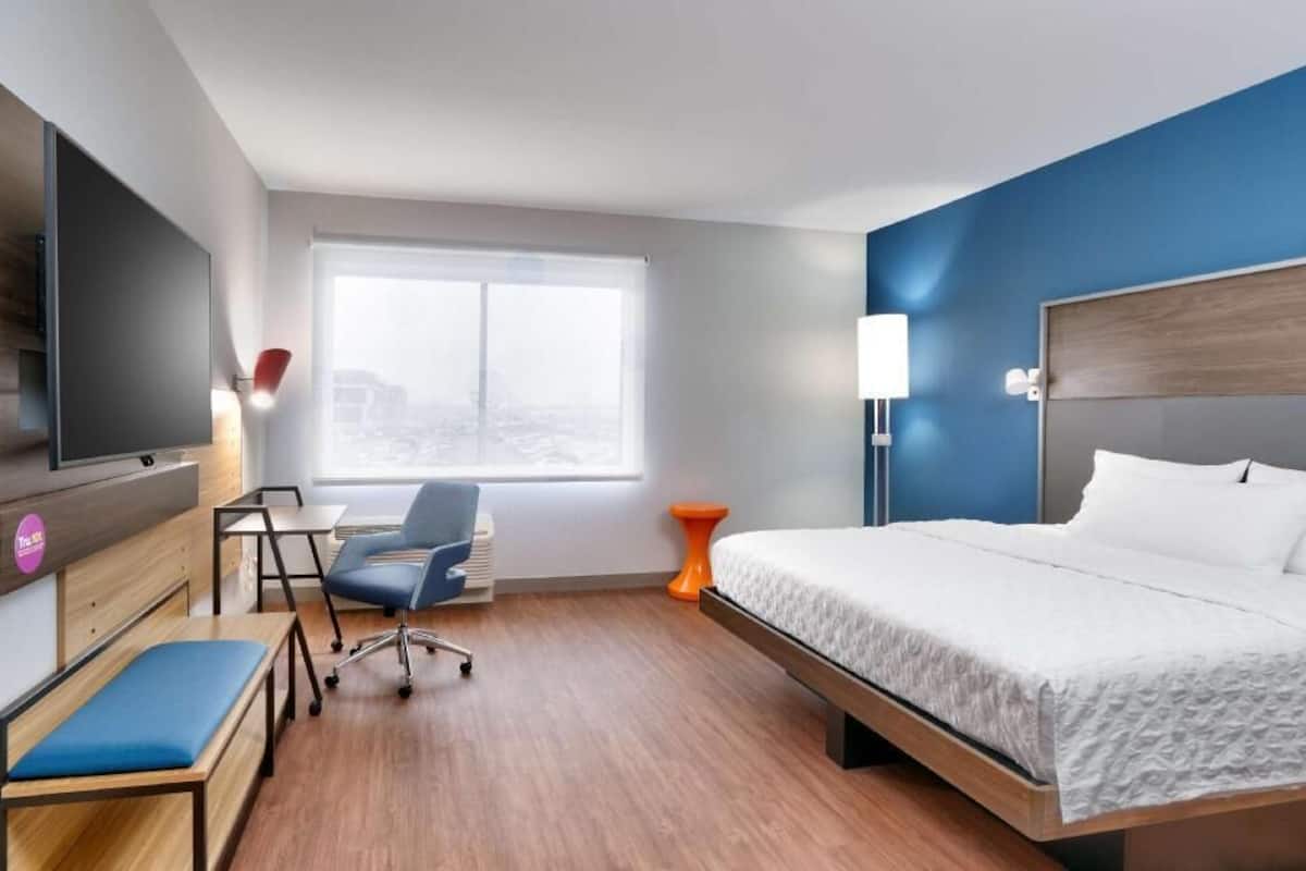 Una habitación de hotel con cama, escritorio, silla, televisor y ventana.