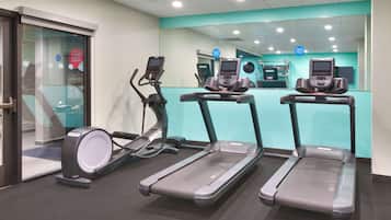 Un gimnasio con cintas de correr, elípticas y un espejo grande.