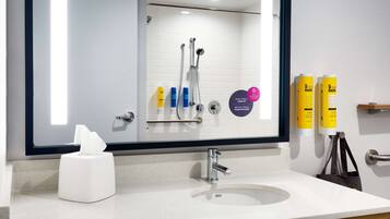 A modern bathroom with a white sink, a mirror, and a shower with a glass door. There are toiletries on the wall and a tissue box on the counter.