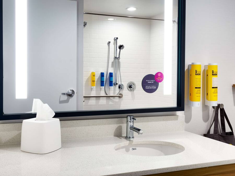 A modern bathroom with a white sink, a mirror, and a shower with a glass door. There are toiletries on the wall and a tissue box on the counter.