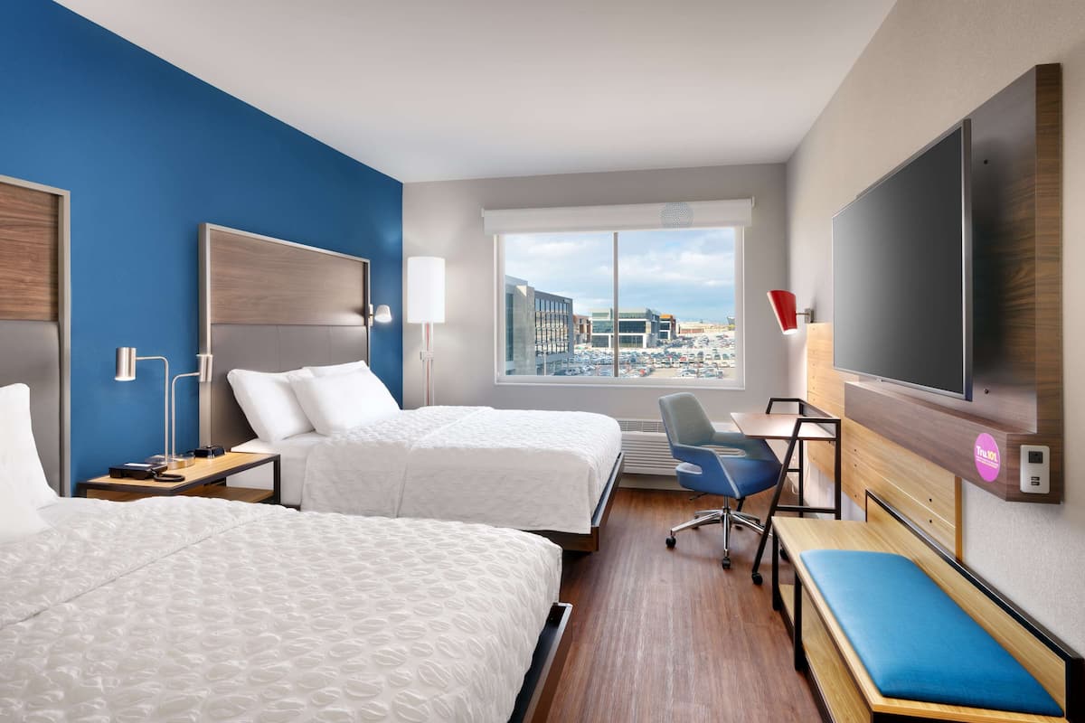 Habitación de hotel con dos camas, un escritorio, una silla, un televisor y una ventana con vista a la ciudad.
