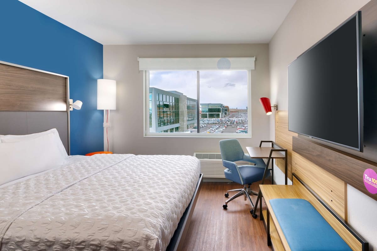 Habitación de hotel con cama, escritorio, silla, televisión y ventana con vista a la ciudad.
