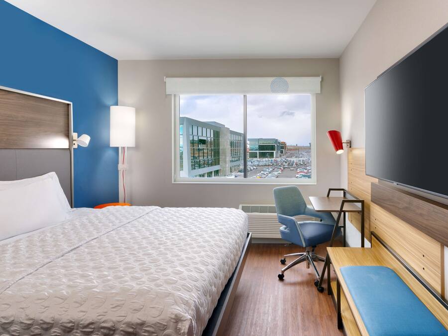 A hotel room with a bed, a desk, a chair, a TV, and a window with a city view.