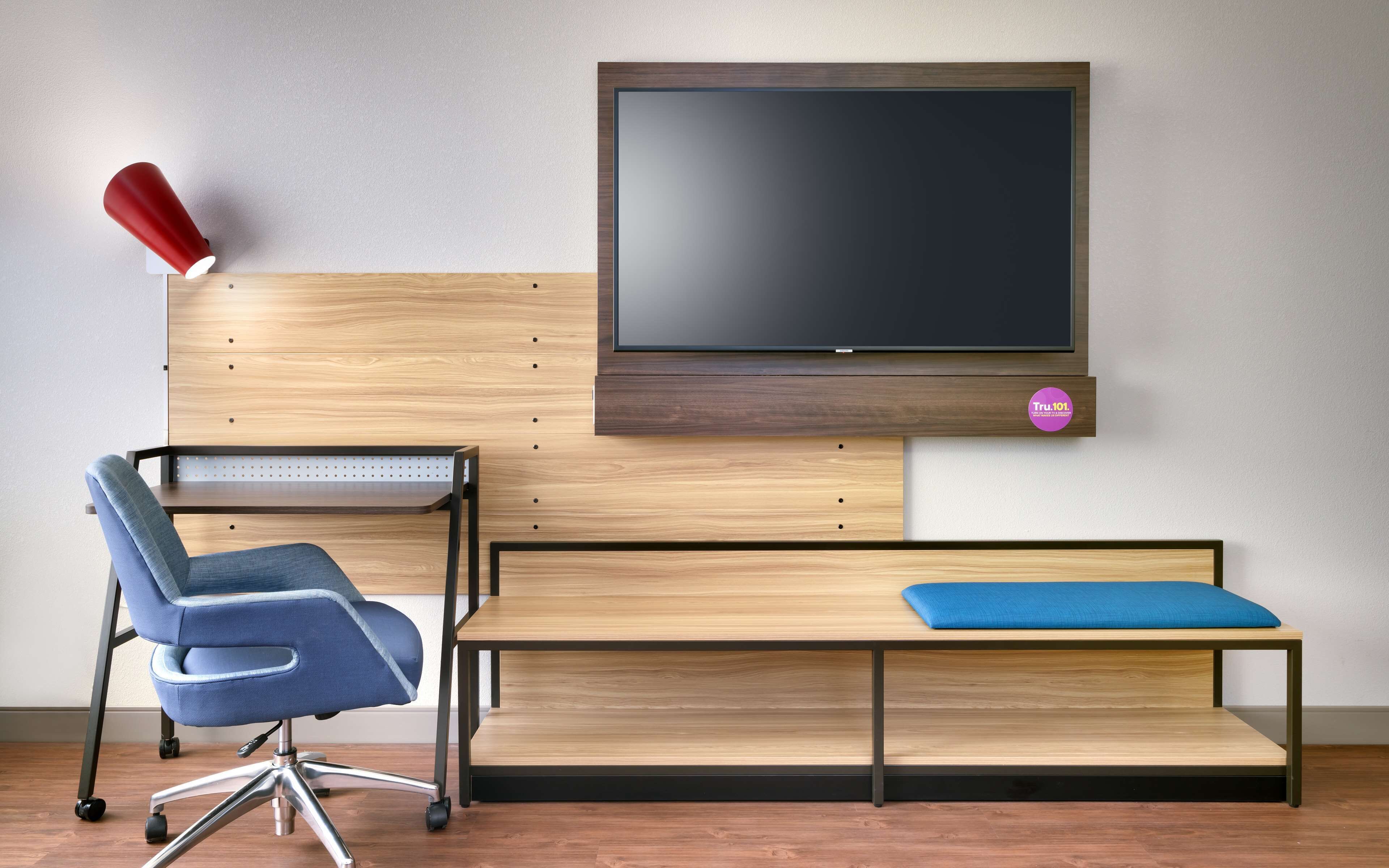 A modern room with a wooden desk, a blue office chair, a red lamp, and a mounted TV.