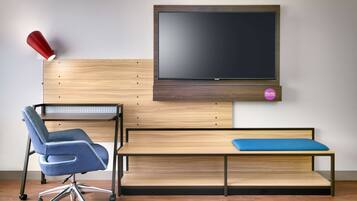A modern room with a wooden desk, a blue office chair, a red lamp, and a mounted TV.
