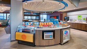 Een moderne zelfbedieningskiosk met diverse drankjes en snacks, een magnetron en een zithoek met uitzicht op de stad.