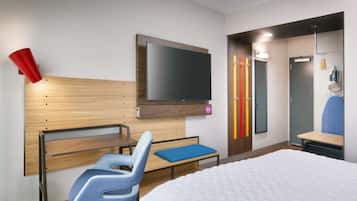 Una habitación de hotel moderna con cama, escritorio, silla, televisor y armario.