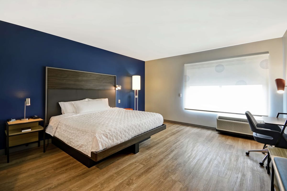 A modern hotel room with a large bed, bedside tables, a desk, and a chair.