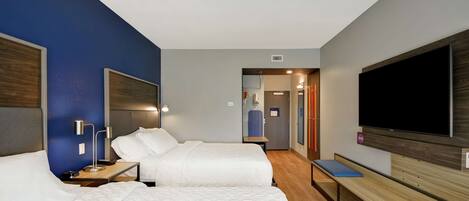Habitación de hotel con dos camas, televisión, un banco y baño visible a través de una puerta abierta.
