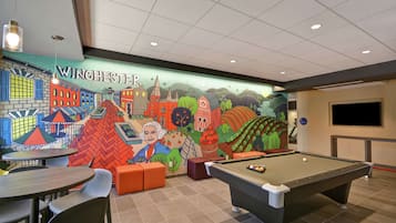 Una mesa de billar en una habitación con un mural que muestra una escena urbana, mesas y sillas.