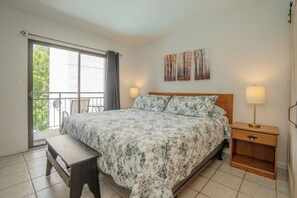 A bedroom with a bed, bedside lamps, a bench, and a view of the outdoors. - Laurel Inn 206 is a beautiful condo with private balcony close to downtown (Gatlinburg)