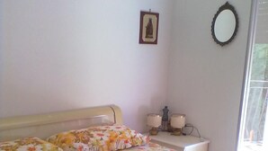 A bedroom with a bed, a bedside table with lamps, a framed picture on the wall, and a window. - Apartment in residence in Mongiove a stone's throw from the sea (Mongiove)