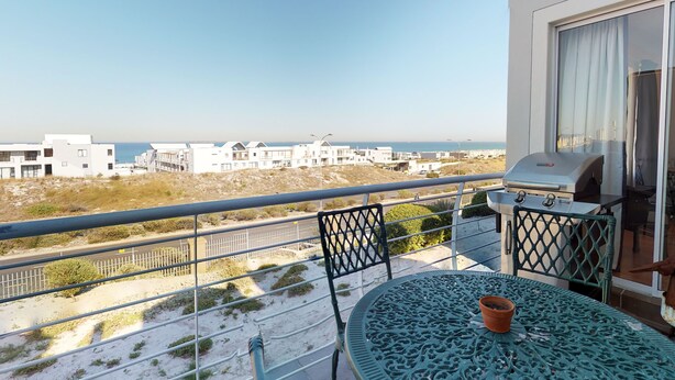 A balcony with a view of the beach and buildings, a grill, and a table with a potted plant. - Copper Den Condo (Cape Town)