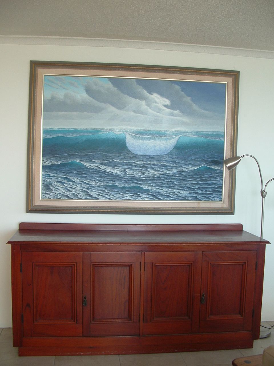 Un tableau encadré représentant une vague, accroché à un meuble en bois.