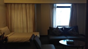 A hotel room with a bed, a sofa, a coffee table, and a window with curtains. - 1 Ivy Suite At Berjaya Times Square (Kuala Lumpur)