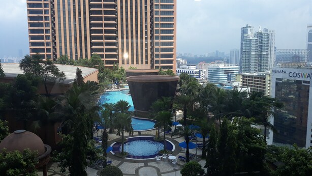 A high-rise building with a pool area featuring a circular water feature, surrounded by palm trees and lounge chairs. - 1 Ivy Suite At Berjaya Times Square (Kuala Lumpur)