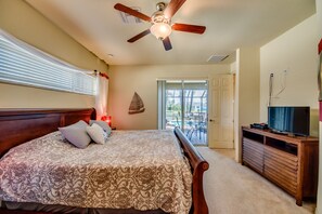 Une chambre avec un lit, un ventilateur de plafond, un téléviseur posé sur un meuble en bois, et une vue sur l’extérieur grâce à une porte vitrée.