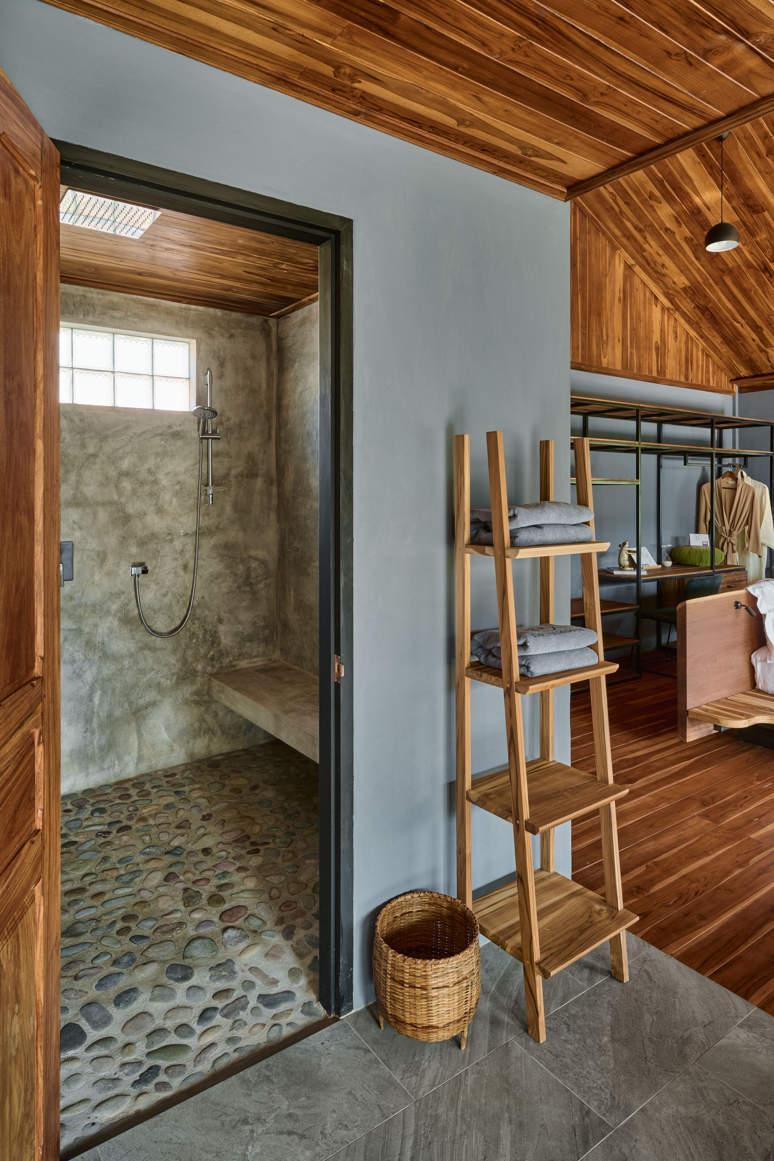 A room with a stone-tiled shower area, a wooden ladder shelf, and a wicker basket.