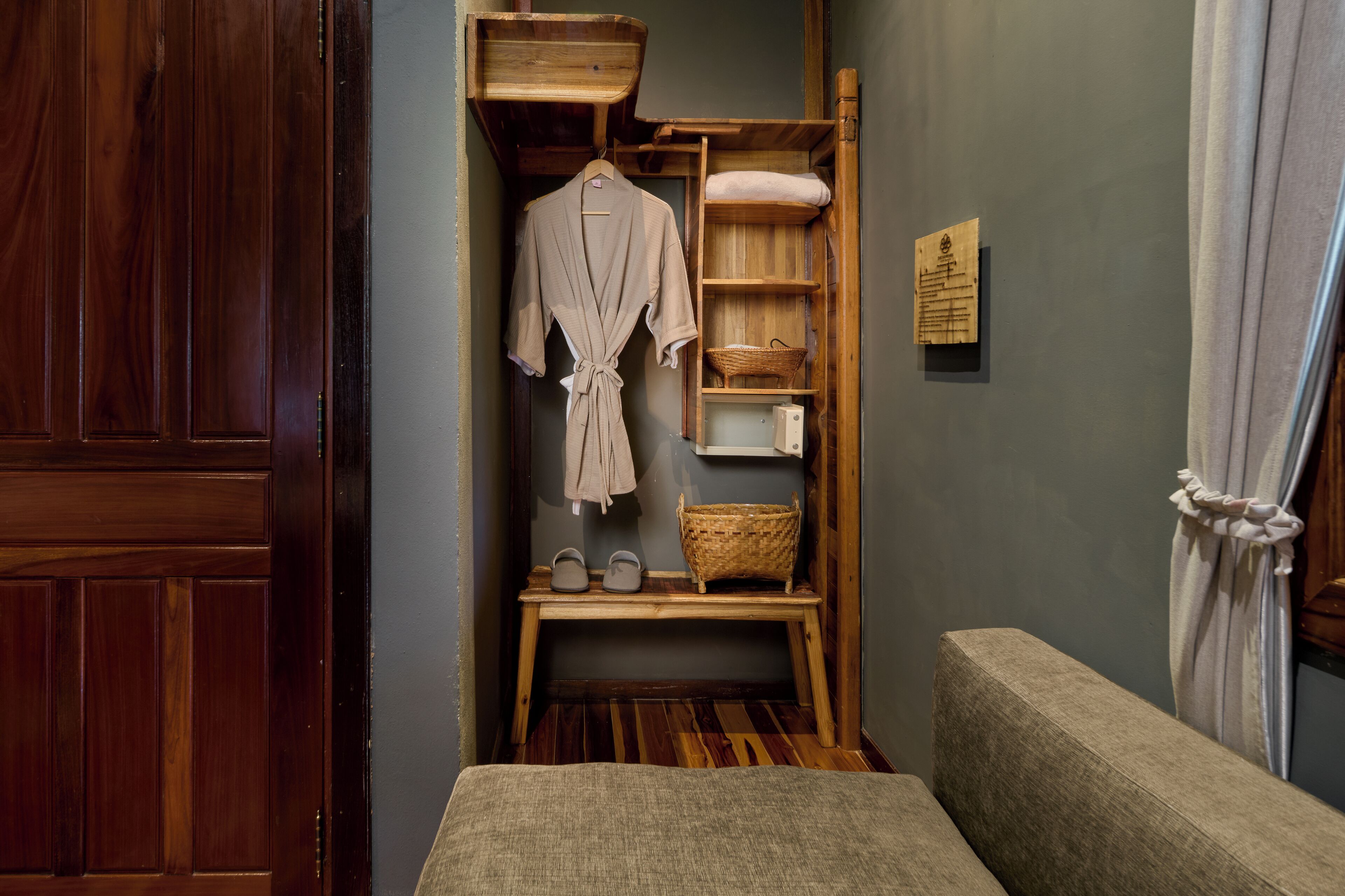 A wooden bench with a woven basket, a wooden shelf with a robe and slippers, and a wooden door.