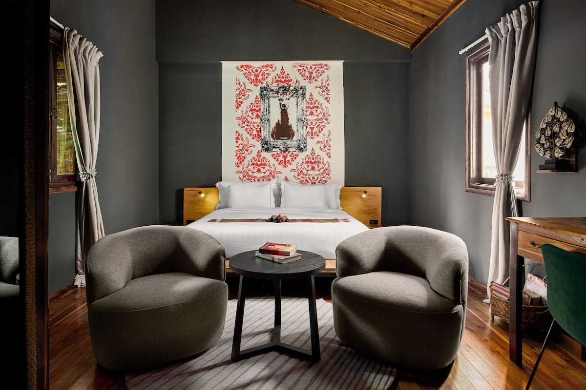 Une chambre à coucher avec un grand lit, deux fauteuils, une petite table et une tapisserie décorative au mur.