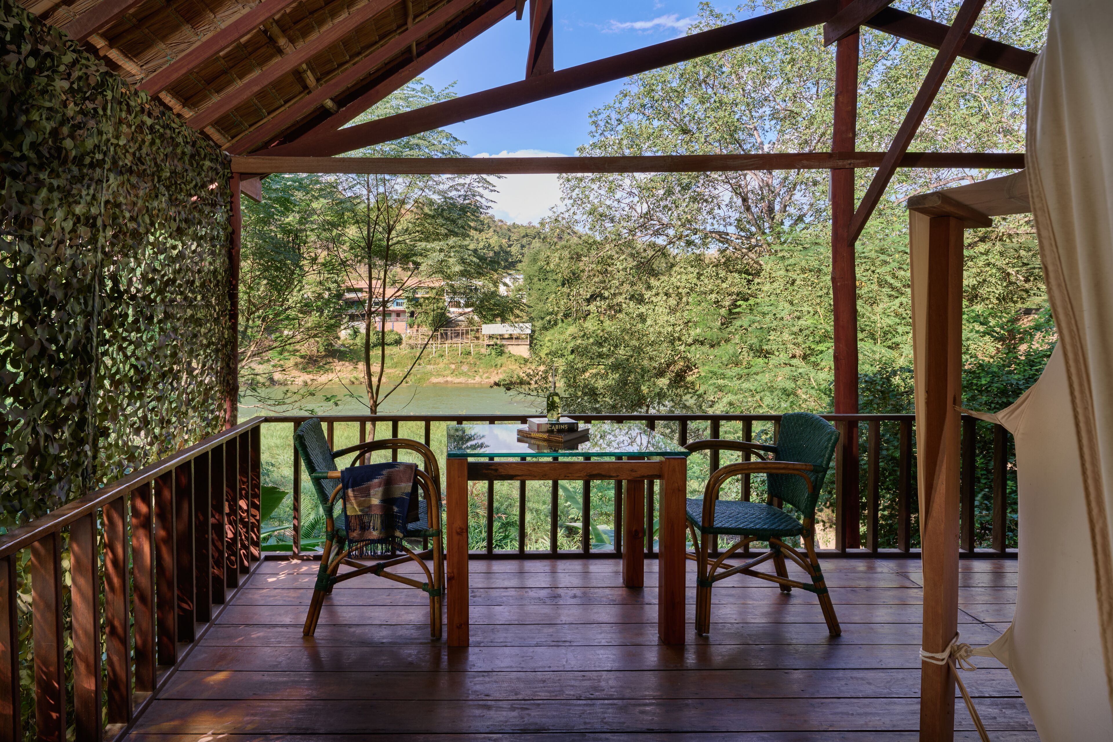 A wooden deck with a table and chairs, overlooking a lush green landscape with trees and a distant building.