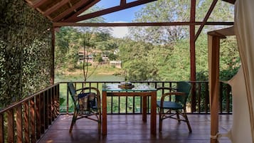 A wooden deck with a table and chairs, overlooking a lush green landscape with trees and a distant building.