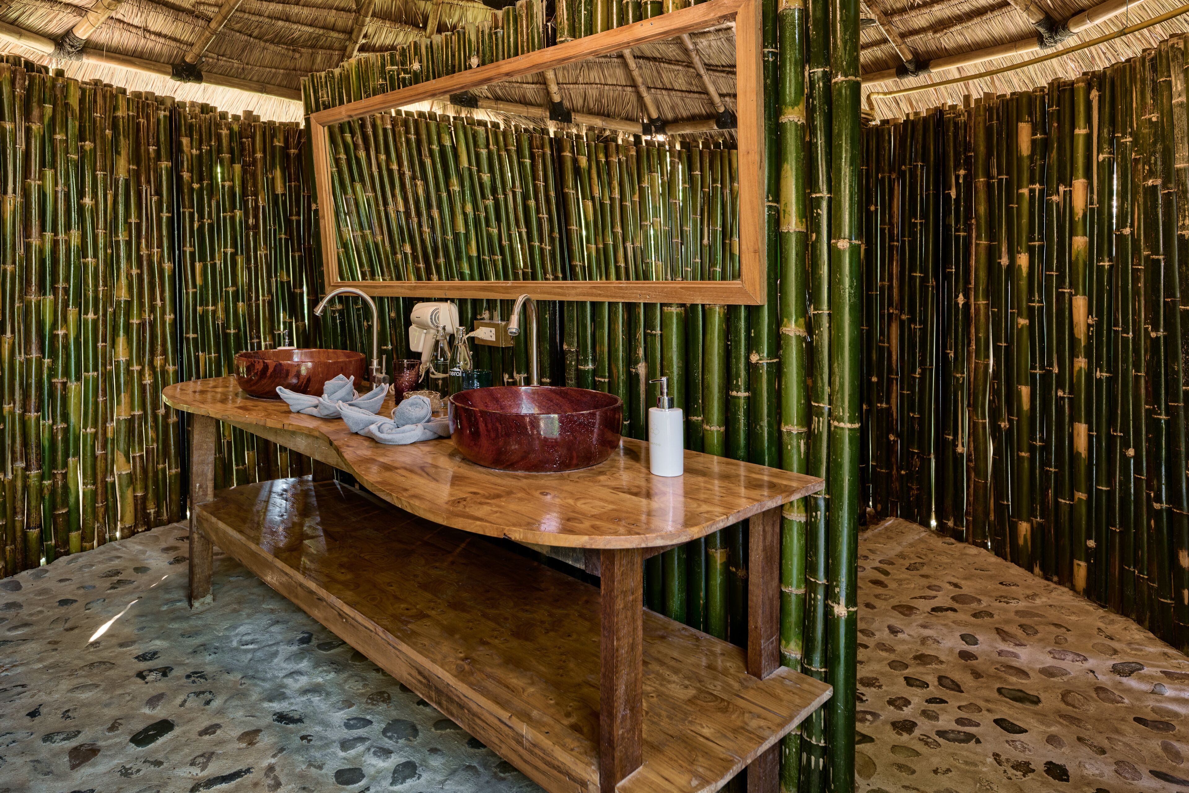Un baño con tocador de madera, un espejo grande y un fondo de bambú.