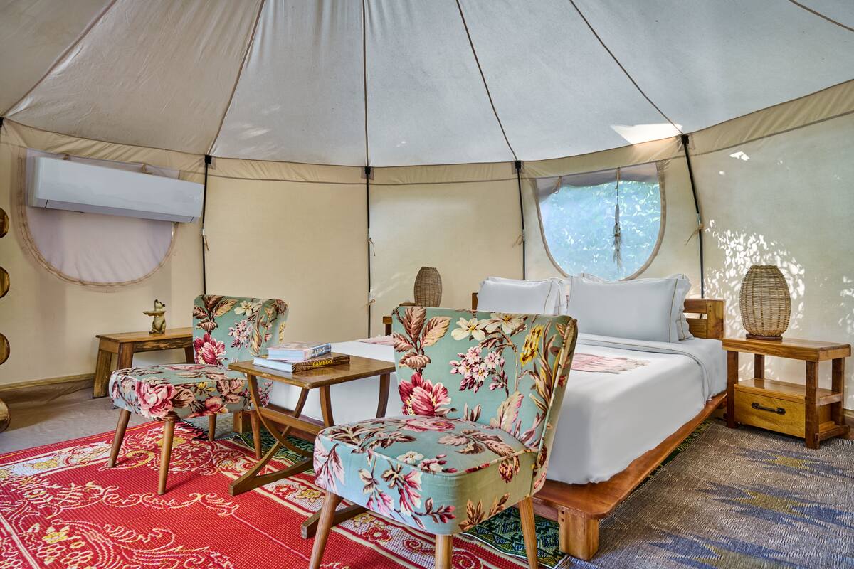 Un hébergement sous tente comprenant un lit, deux chaises, une petite table et une fenêtre.