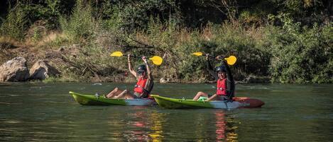 Dos personas remando en kayak por un río tranquilo, rodeado de abundante vegetación.