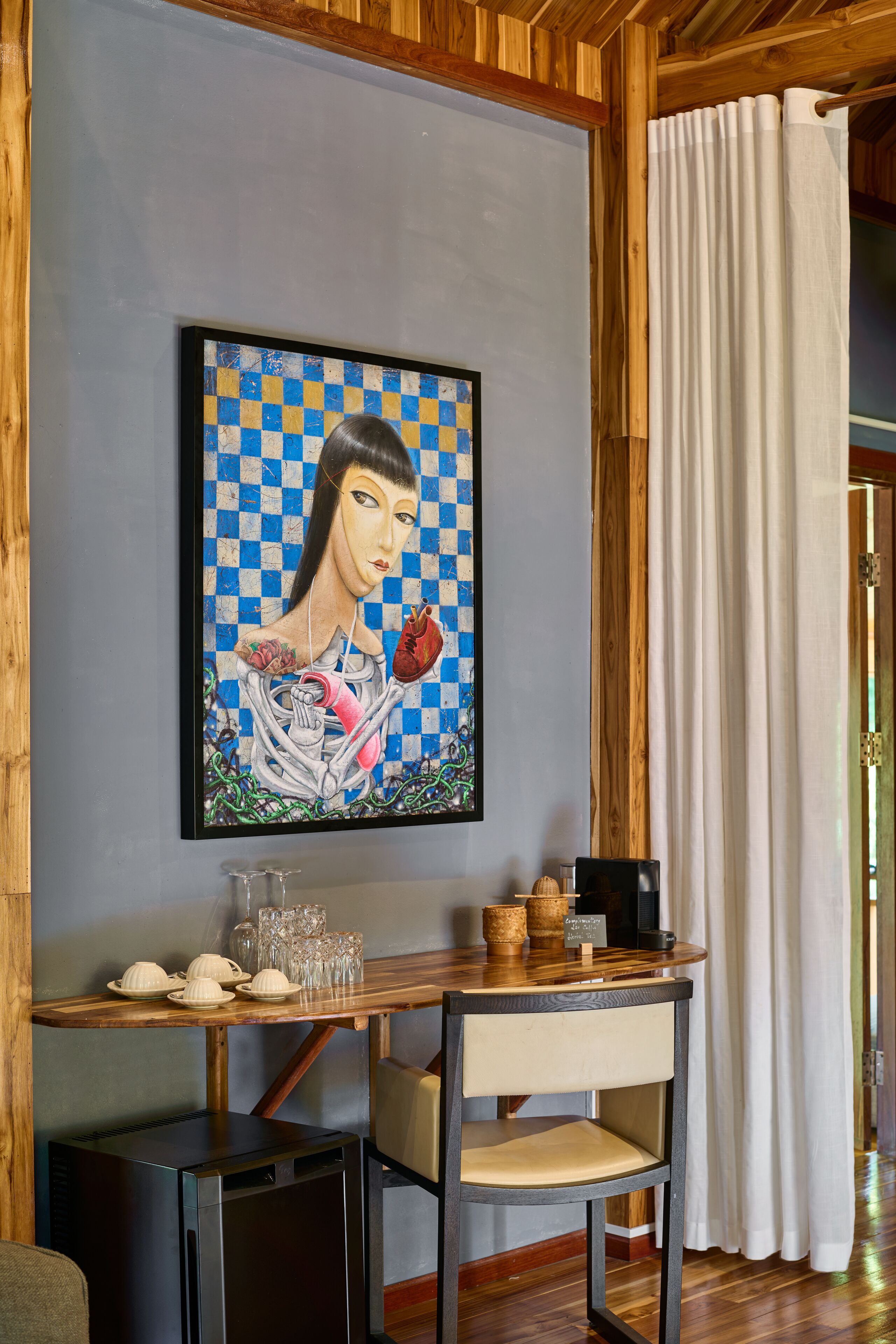 A framed artwork on a wall, a table with a chair, and a small refrigerator.