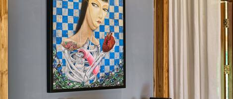 A framed artwork on a wall, a table with a chair, and a small refrigerator.