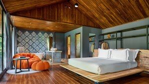 A modern bedroom with a wooden ceiling, a large bed, orange bean bag chairs, and a view of the outdoors. - The Namkhan, a Small Luxury Hotel of the World (Luang Prabang)