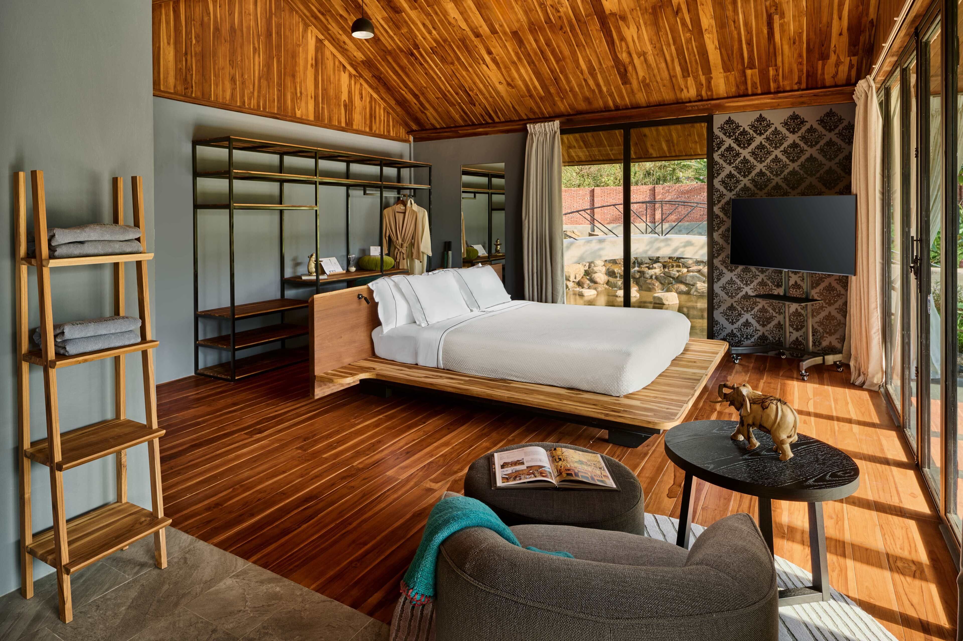 A modern bedroom with a wooden floor, a bed, a TV, and a large window.