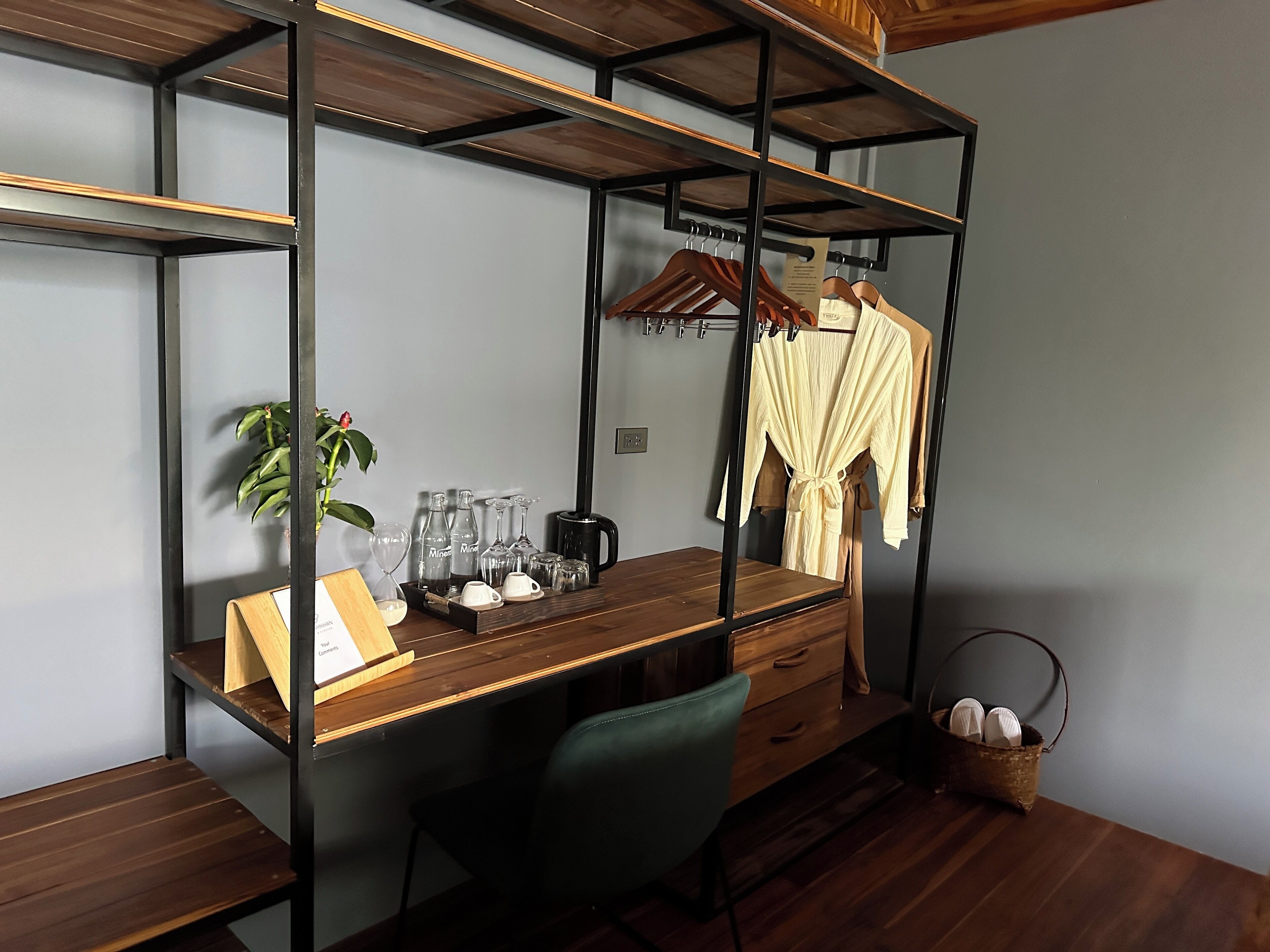 A compact room with a wooden desk, a chair, a hanging robe, and a small plant.