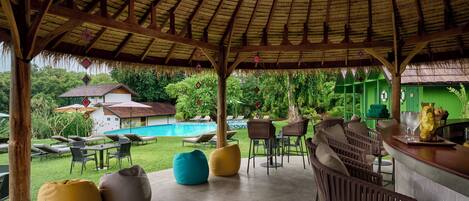 An outdoor bar area with seating and a pool in the background.