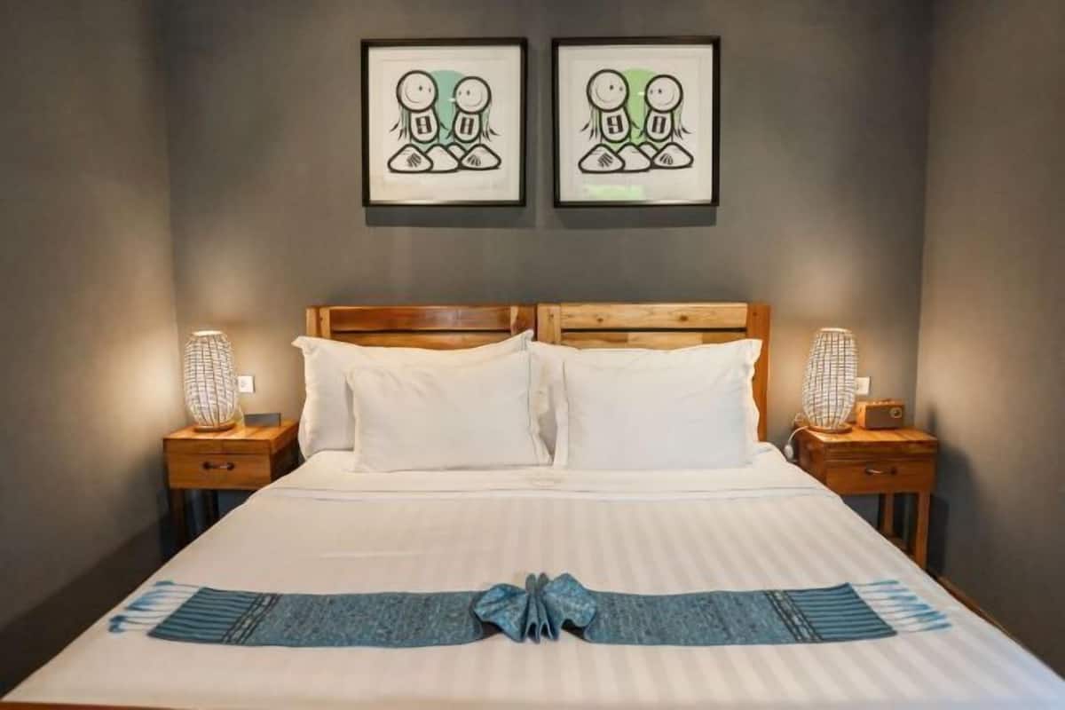 Un lit bien fait, avec du linge de lit blanc, deux œuvres d’art encadrées au-dessus, et un nœud décoratif bleu sur la couverture.